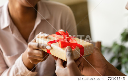 Unrecognizable black guy giving his girlfriend birthday gift at cafe, closeup of hands Unrecognizable black guy giving his girlfriend birthday gift at cafe, closeup of hands 72105545
