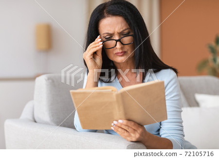 Mature woman touching glasses trying to read book 72105716