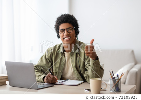 Positive black student in headset gesturing thumb up near laptop at home 72105923