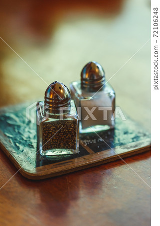 Salt and black pepper in shakers on a table Salt and black pepper in shakers on a table 72106248