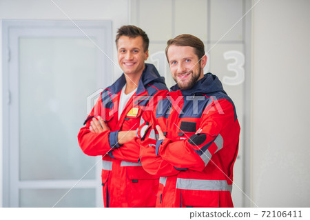 Two medical workers in red uniform standing with arms crossed 72106411