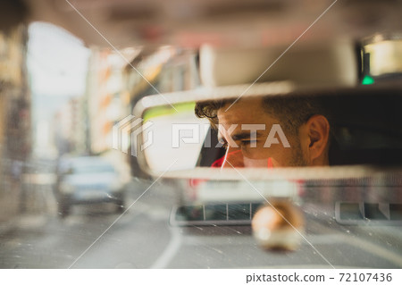 View of a man on the rearview mirror of a car 72107436