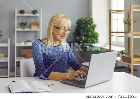 Inspired mature woman working on laptop, writing book or posting article on her blog Inspired mature woman working on laptop, writing book or posting article on her blog 72111656