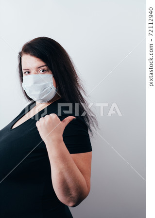 Woman in medical mask pointing thumb on copy space Woman in medical mask pointing thumb on copy space 72112940