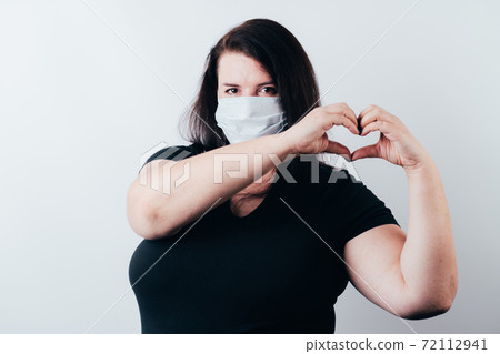 Young woman in medical mask making heart gesture Young woman in medical mask making heart gesture 72112941