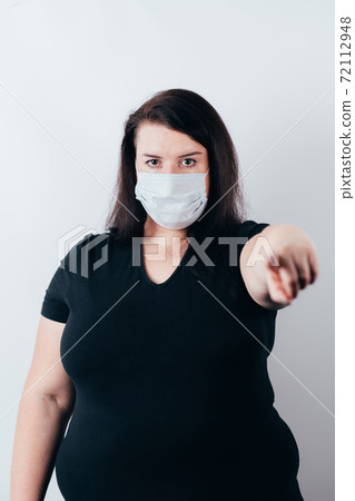 Woman in mask pointing finger looking at camera 72112948