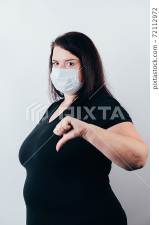 Woman in medical mask showing thumb down gesture 72112972