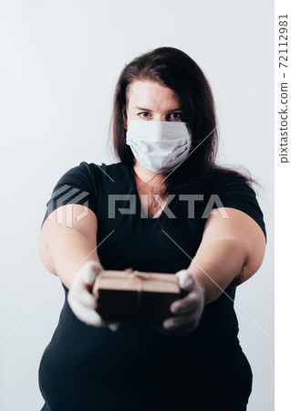 Woman in a face mask and gloves giving a gift box Woman in a face mask and gloves giving a gift box 72112981