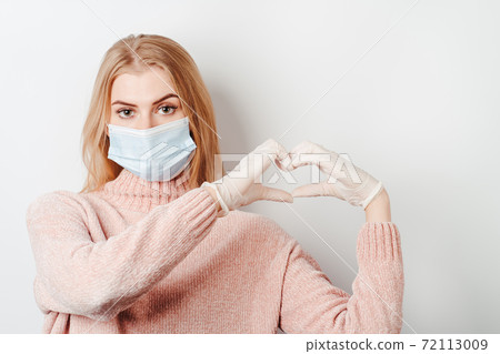 Young woman in medical mask making heart gesture 72113009
