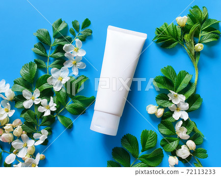 Unbranded white squeeze cosmetic tube, spring flowers and leaves on bright blue background. Natural organic spa cosmetics concept. Flatlay lifestyle, mockup, top view. Unbranded white squeeze cosmetic tube, spring flowers and leaves on bright blue background. Natural organic spa cosmetics concept. Flatlay lifestyle, mockup, top view. 72113233