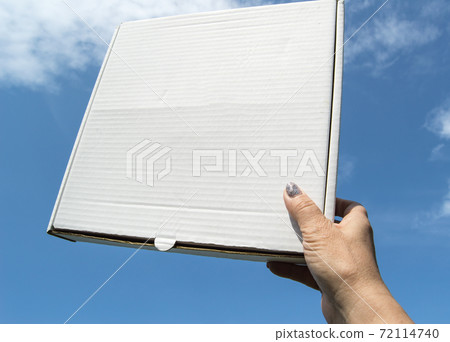 A woman's hand holds a white cardboard box with a copy of the space and space for text on a blue sky background, template, mockup A woman's hand holds a white cardboard box with a copy of the space and space for text on a blue sky background, template, mockup 72114740