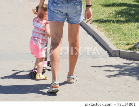 Young mother with bare legs, in shorts, walks with her little daughter in the Park, in the summer, outdoors 72114801