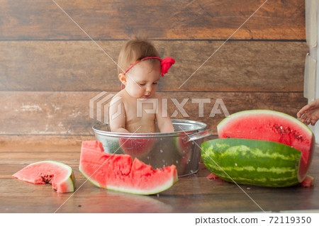One year old baby girl eats watermelon.  72119350