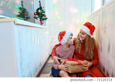 Smiling funny two children in Santa red hat holding Christmas gift in hand. New year concept. Smiling funny two children in Santa red hat holding Christmas gift in hand. New year concept. 72120714