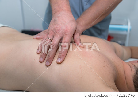 Masseur gives therapeutic massage to man. Male hands do massage of back to patient man. Male patient having massage in clinic. Man relaxing on massage table Masseur gives therapeutic massage to man. Male hands do massage of back to patient man. Male patient having massage in clinic. Man relaxing on massage table 72123770