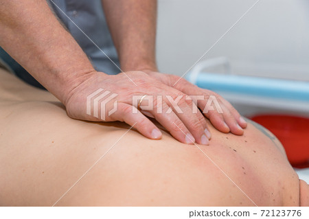 Masseur gives therapeutic massage to man. Male hands do massage of back to patient man. Male patient having massage in clinic. Man relaxing on massage table 72123776