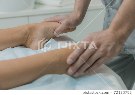 Male hands do massage of legs to patient girl. Young woman having massage in cosmetology clinic. Woman relaxing on massage table 72123792