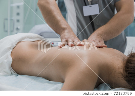 Young woman having massage in cosmetology clinic. Close-up of woman relaxing during back massage lying on massage table. Masseur gives a therapeutic massage to a beautiful woman. Young woman having massage in cosmetology clinic. Close-up of woman relaxing during back massage lying on massage table. Masseur gives a therapeutic massage to a beautiful woman. 72123799