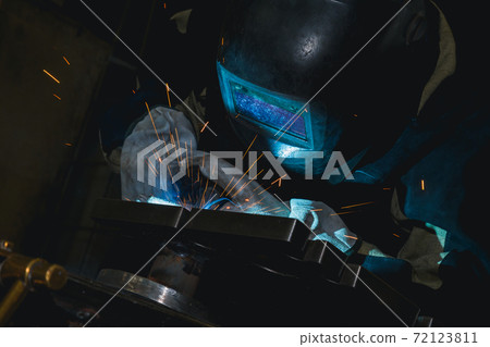 Close-up blacksmith welder in protective mask works with metal steel and iron using a welding machine, bright sparks and flashes. Welder uses a mask to protect your eyes from sparks. 72123811
