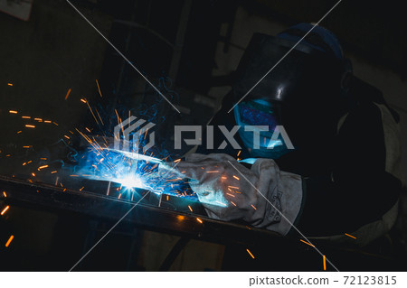 The worker with the welding mask inside the factory. The welding process of a part of the equipment inside the factory The worker with the welding mask inside the factory. The welding process of a part of the equipment inside the factory 72123815