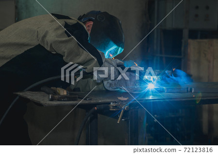 Industrial worker in protective mask using modern welding machine for welding metal construction on production manufacture at metalworking factory. Industrial worker in protective mask using modern welding machine for welding metal construction on production manufacture at metalworking factory. 72123816