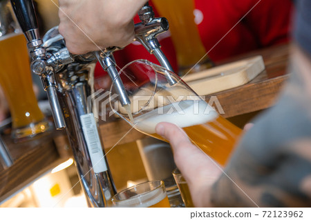 Filling glass with beer. Bartender hand at beer tap pouring draught beer in glass serving in restaurant or pub. Close-up of male barman hand at beer tap pouring lager beer at restaurant or bistro. Filling glass with beer. Bartender hand at beer tap pouring draught beer in glass serving in restaurant or pub. Close-up of male barman hand at beer tap pouring lager beer at restaurant or bistro. 72123962