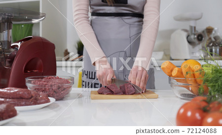 Woman cutting raw meat on small pieces with kitchen knife cutting board. Female cutting red beef filet on wooden board, holding knife in hand. Housewife is cooking at home interior. Concept: food 72124088