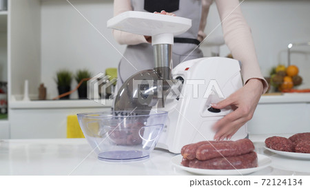 Making minced meat in electric meat grinder from fresh beef at home. Electric mincer machine with fresh chopped meat. Preparation of minced beef with electric grinder. Written on apron: best recipes 72124134
