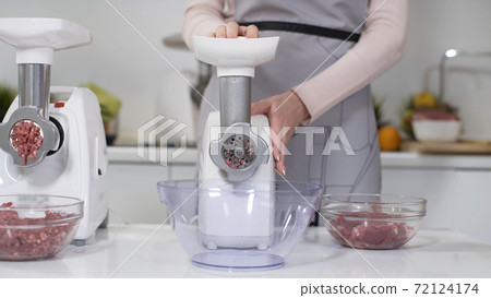 Making raw mincemeat with meat mincer at home. Pile of chopped meat. Electric mincer machine with fresh chopped meat. Preparation of minced beef with an electric meat grinder. 72124174