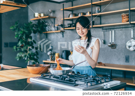 烹調的婦女，當觀看智能手機時 72126934