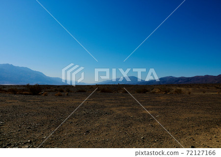 Bright sunny view over Death Valley from Hell's Gate viewpoint in a landscaped of scattered rocks and shrubs - California. Bright sunny view over Death Valley from Hell's Gate viewpoint in a landscaped of scattered rocks and shrubs - California. 72127166