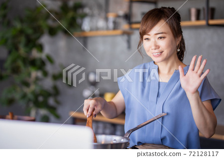 A woman who cooks while watching a computer A woman who cooks while watching a computer 72128117