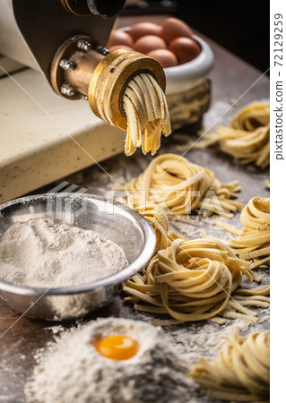Flour, eggs and a pasta maker producing fresh Italian fettuccine 72129259