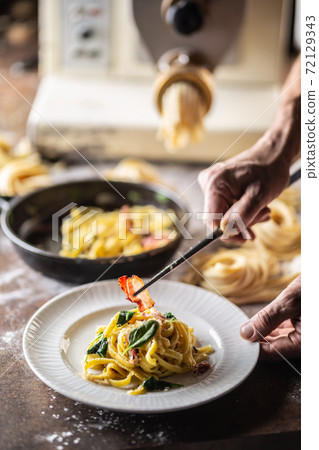 Hands of chef plating freshly cooked pasta with a pasta maker in the background 72129343