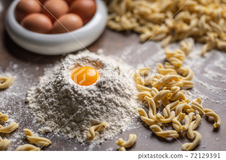 Pile of flour with an egg yolk and fresh pasta on a cooking desk Pile of flour with an egg yolk and fresh pasta on a cooking desk 72129391