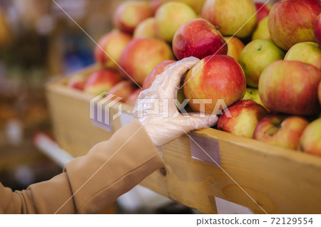 Close-up of females hand in protective gloves hold beautiful fresh apple in hand. Shopping during quarantine 72129554