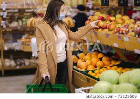Female buyer wearing a protective mask and gloves in supermarket. Shopping during the pandemic quarantine. Woman buying fresh fruits Female buyer wearing a protective mask and gloves in supermarket. Shopping during the pandemic quarantine. Woman buying fresh fruits 72129609