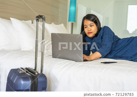 Working on laptop while lying on bed next to suitcase Working on laptop while lying on bed next to suitcase 72129783