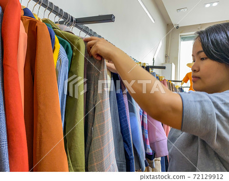 Asian woman hanging clothes on hanger at retail store Asian woman hanging clothes on hanger at retail store 72129912