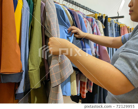Woman choosing outfit while shopping at fashion clothes store 72129955
