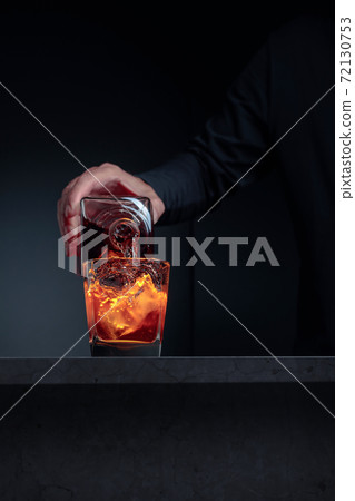 Alcoholic drink pouring from a bottle into a frosted glass with ice. Alcoholic drink pouring from a bottle into a frosted glass with ice. 72130753