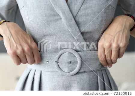 Woman straightening her belt on gray dress with her hands close-up Woman straightening her belt on gray dress with her hands close-up 72130912