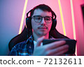 Close up portrait of a boy relaxing playing games on mobile phone and sitting in a gaming chair. Room with colorful neon light 72132611