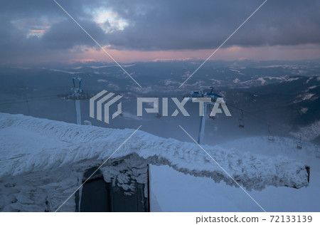 Alpine resortr ski lift with seats going over the sunset mountain skiing slopes in extremally windy weather Alpine resortr ski lift with seats going over the sunset mountain skiing slopes in extremally windy weather 72133139
