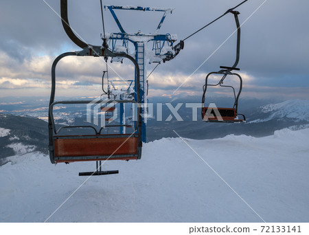Alpine resortr ski lift with seats going over the sunset mountain skiing  slopes in extremally windy weather 72133141