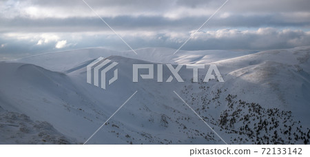 Snow covered winter mountains in last evening sunlight. Magnificent windy dusk on tops above picturesque alpine ski resort Snow covered winter mountains in last evening sunlight. Magnificent windy dusk on tops above picturesque alpine ski resort 72133142