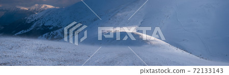 Snow covered mountain slope in last evening sunlight. Magnificent windy dusk on tops above picturesque alpine ski resort, Dragobrat, Ukraine, Carpathian Mountains. 72133143