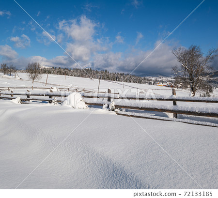 Alpine mountain snowy winter fir forest and snow drifts near wood fence on secondary countryside road wayside 72133185