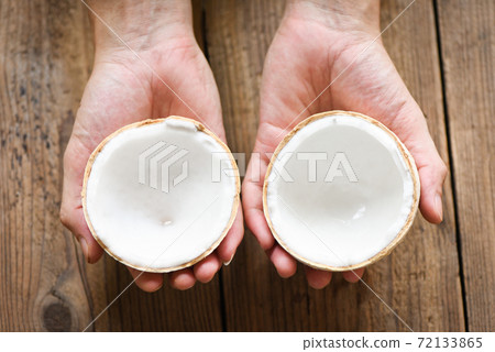 cut half coconut in hand and fresh coconuts on old wooden table for food. 72133865