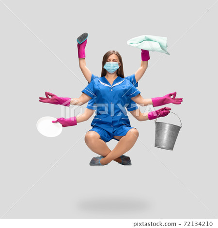 Female housemaid in pink gloves and blue uniform multitask like shiva isolated on gray background. Safety during COVID-19 72134210